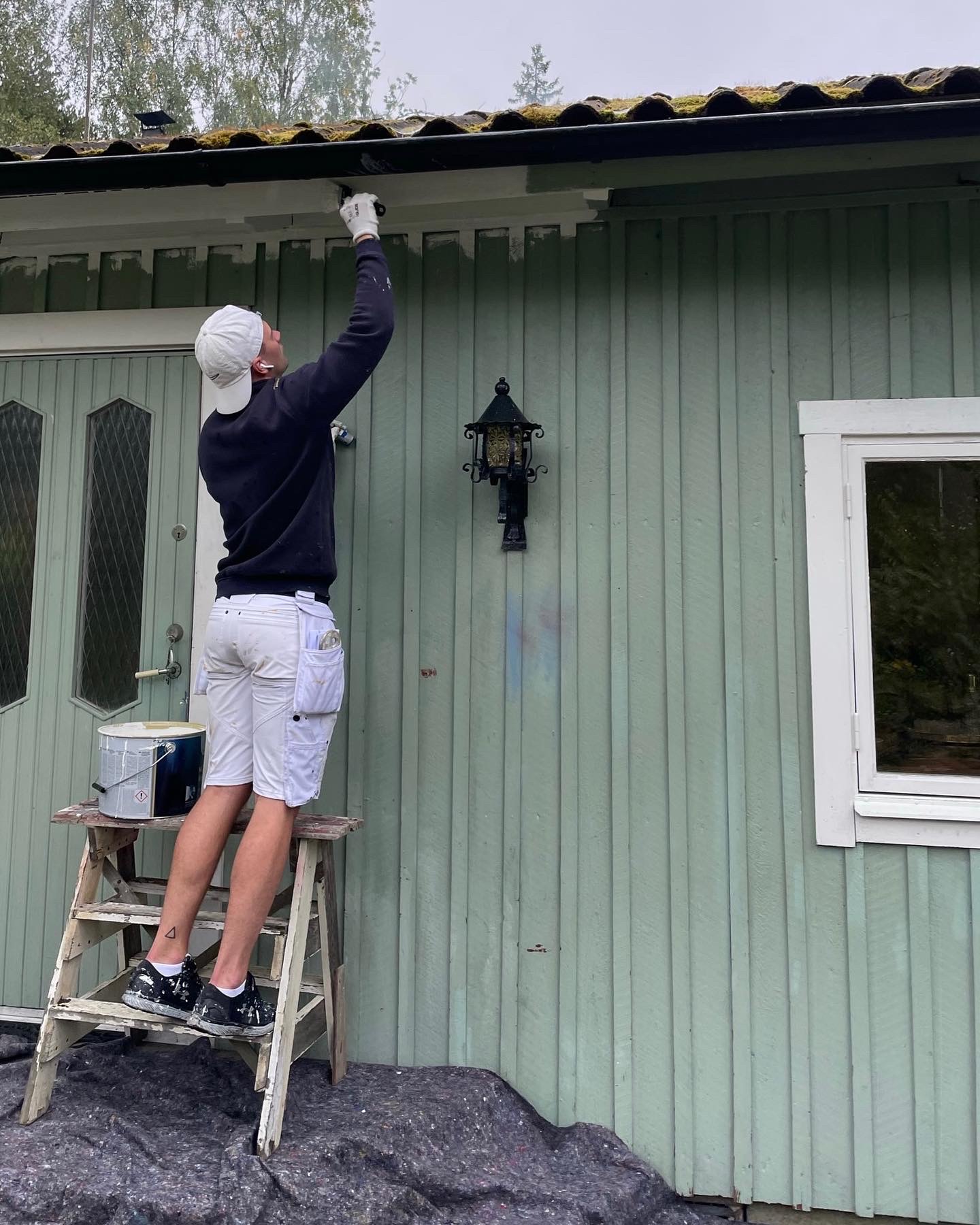 Målare som målar en ljusgrön träfasad