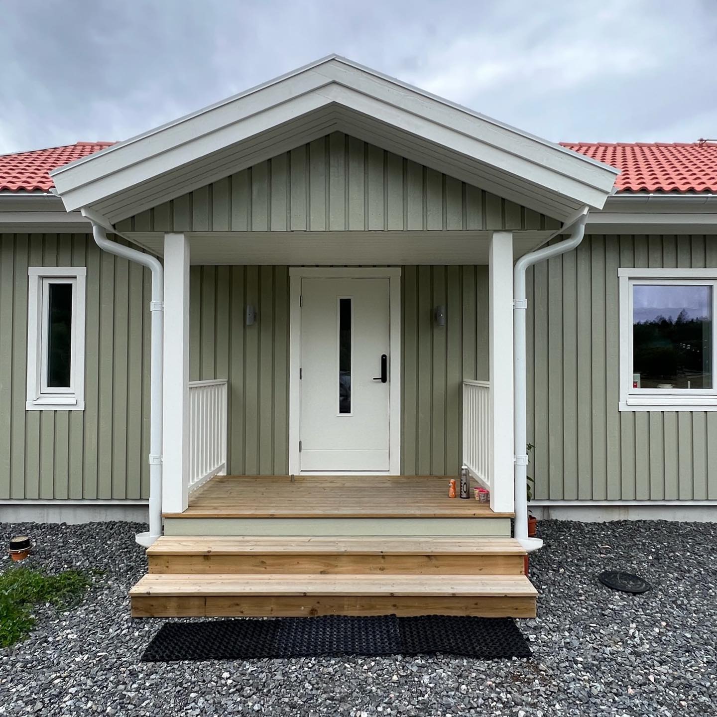 Entré med skärmtak på grönmålat trähus, vit ytterdörr, vita stolpar och räcken samt trätrappa