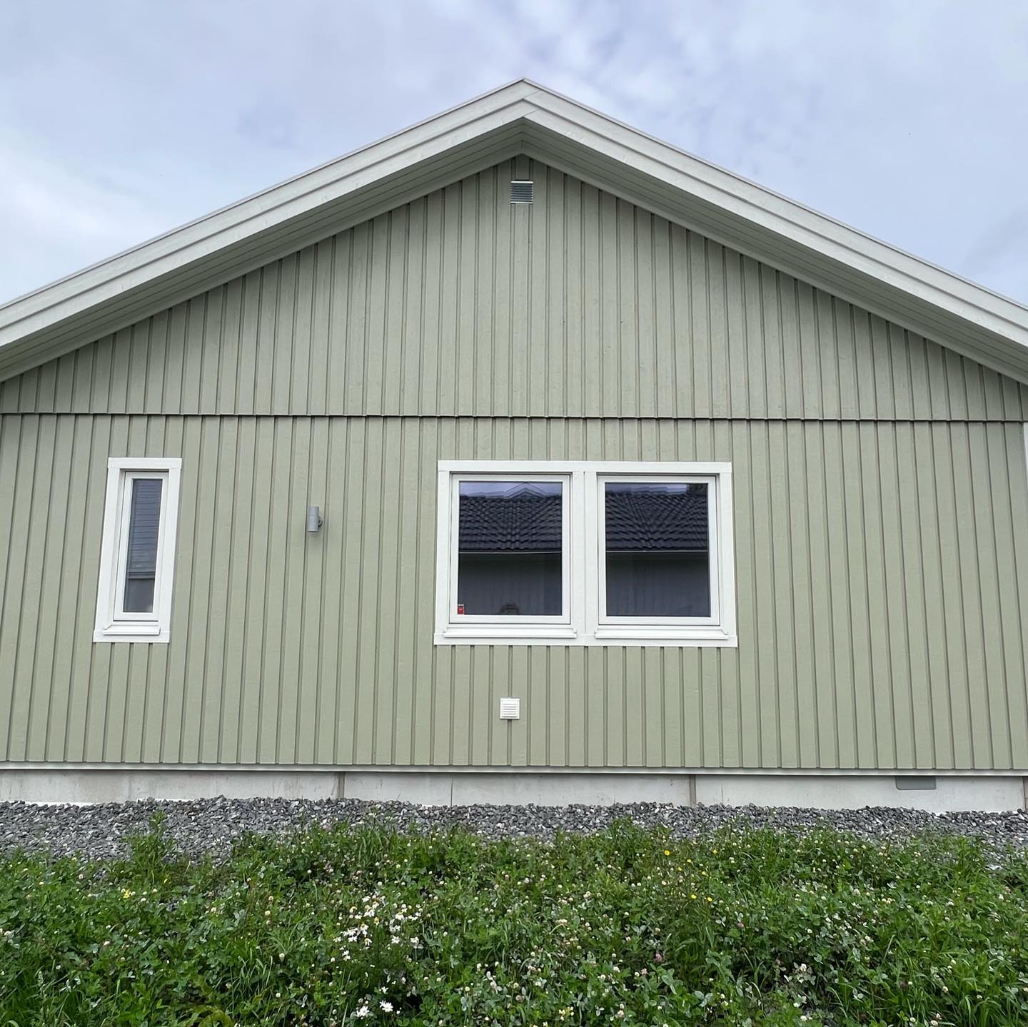 Gavel i grönmålad stående träpanel med vita fönster och vita vindskivor efter målningen