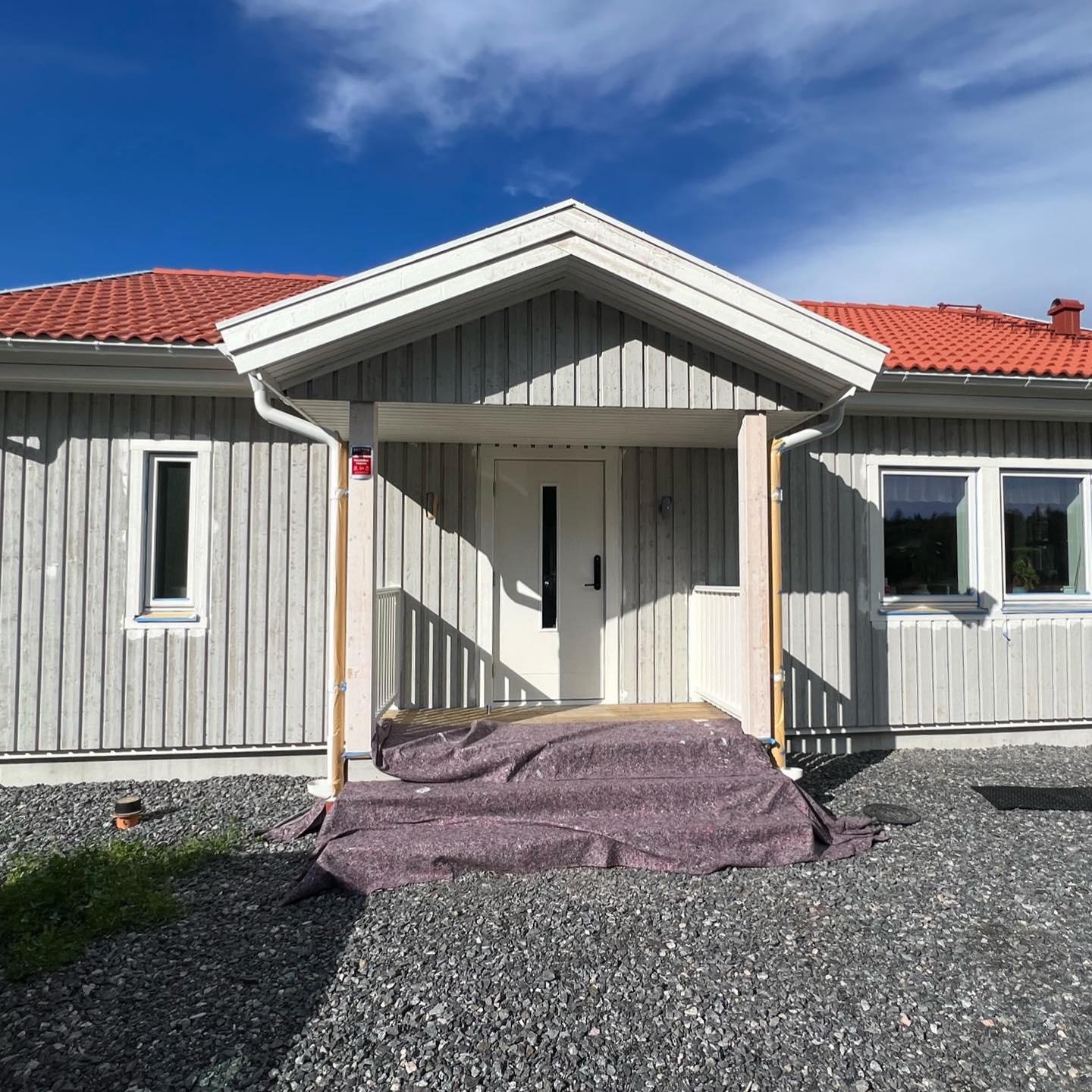 Entré med skärmtak på grått trähus före målning, med skyddstäckt trappa framför ytterdörren