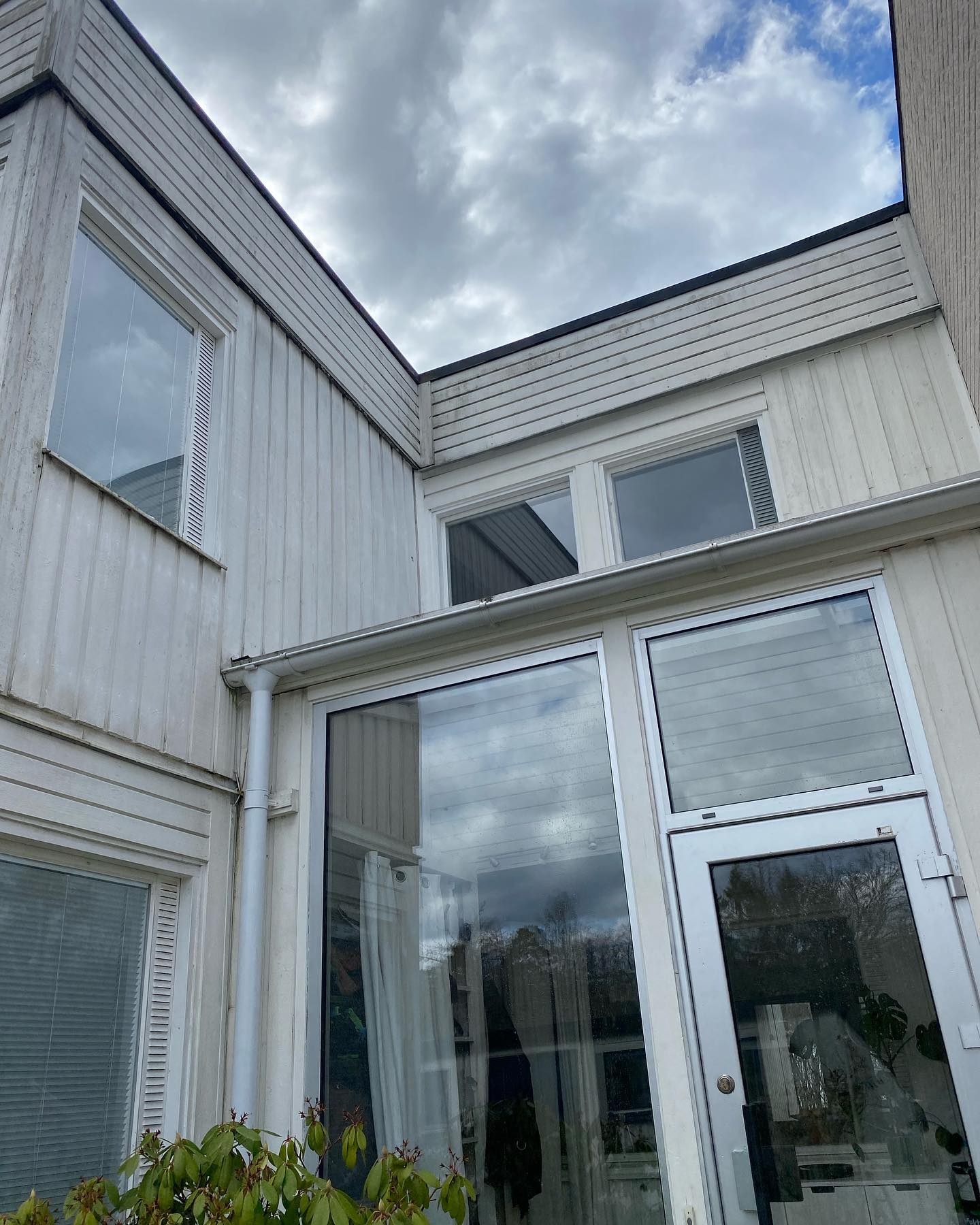 Samma fasadparti med grånad och sliten träpanel kring entrén och de stora glaspartierna