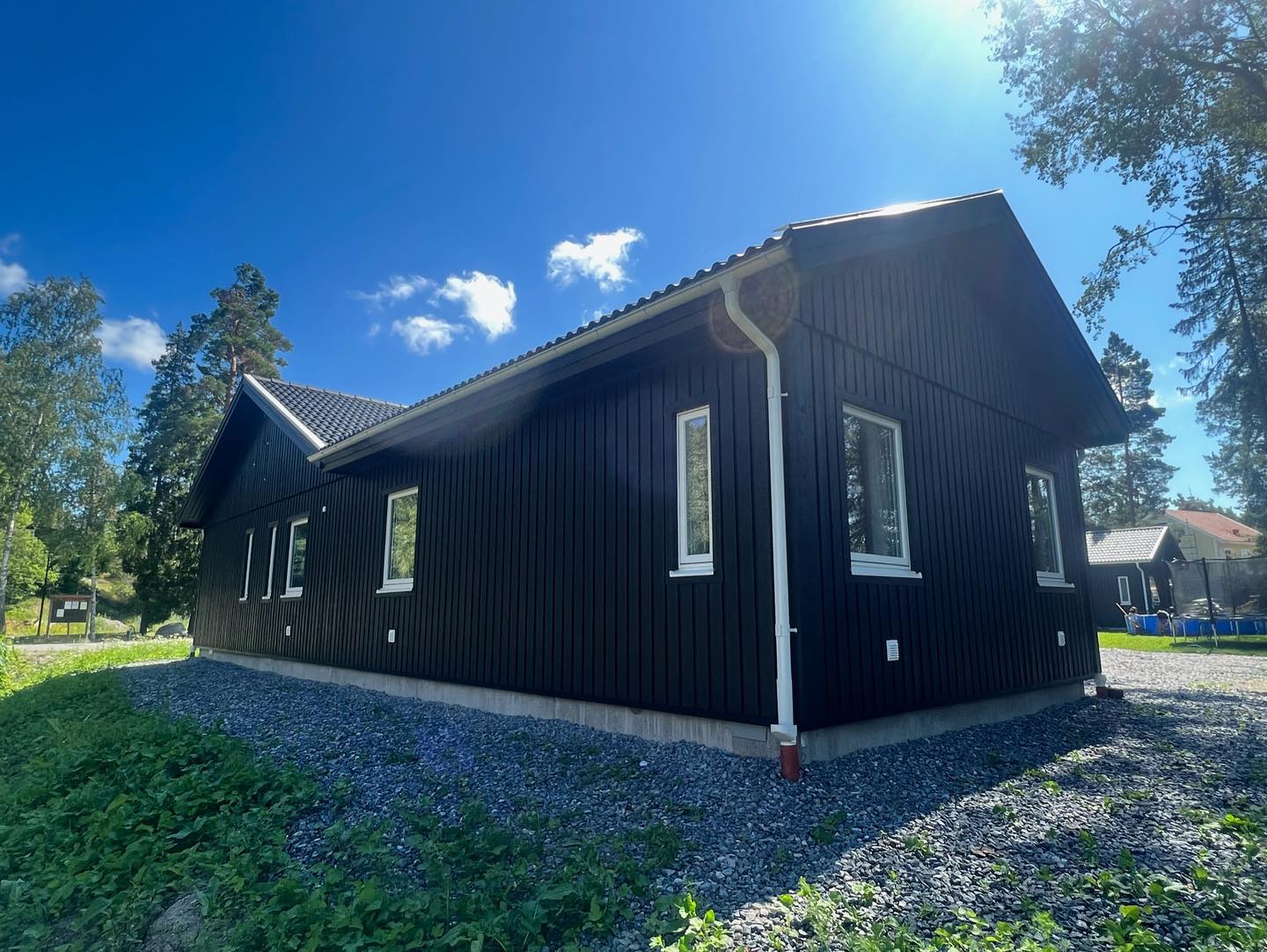 Gavel och långsida på svart träfasad med vita fönsterfoder och vitt stuprör i sol