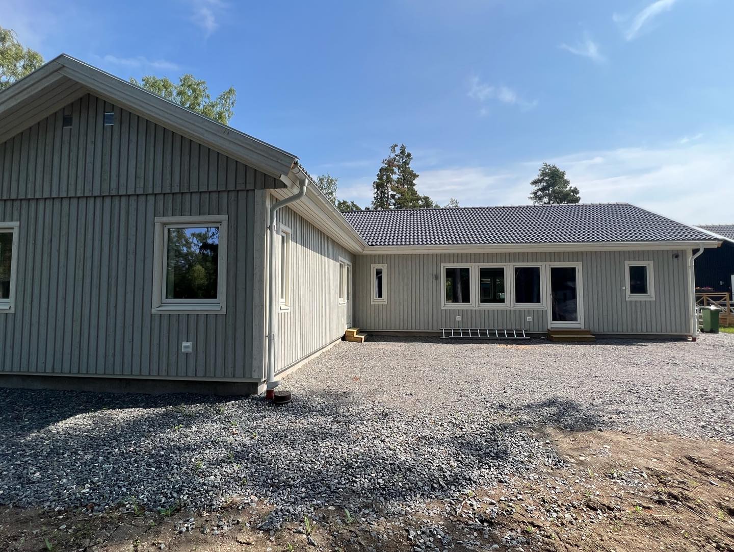 Vinkelbyggd villa med ljusgrå stående träpanel, vita fönster och glasad altandörr efter målning