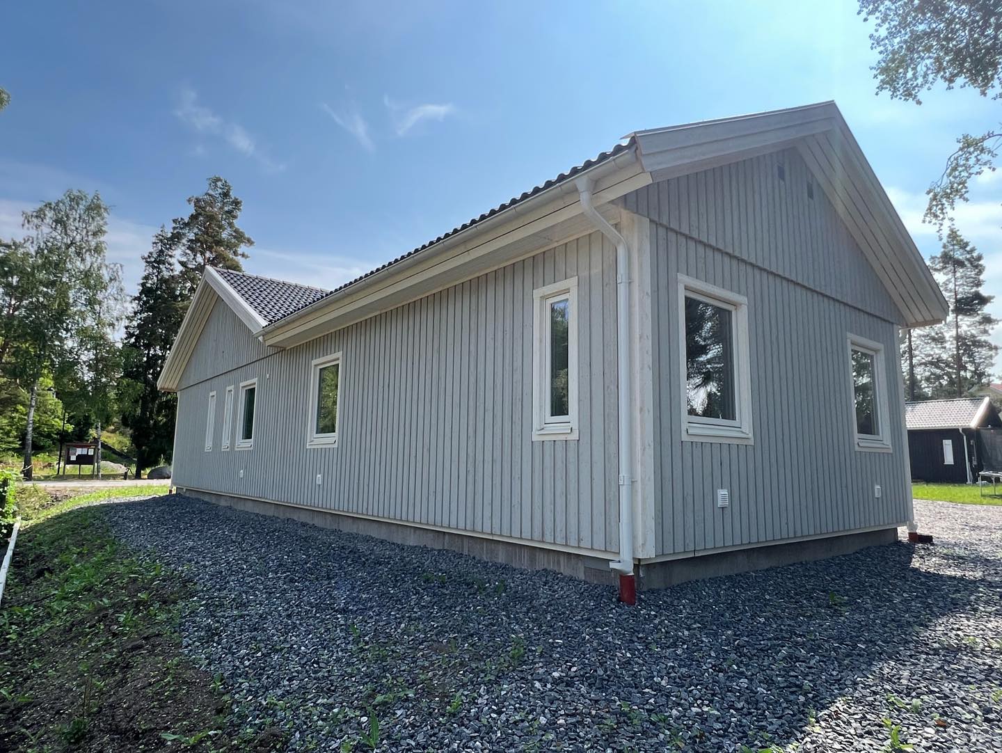 Gavel och långsida på ljusgrå träfasad med vita fönster, vindskivor och stuprör