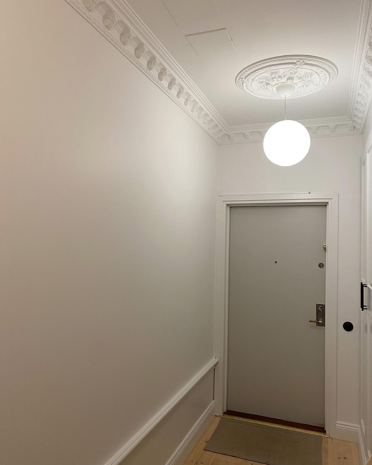 Smal hall med vita väggar, takrosett, takstuckatur och vit bröstlist fram mot entrédörren