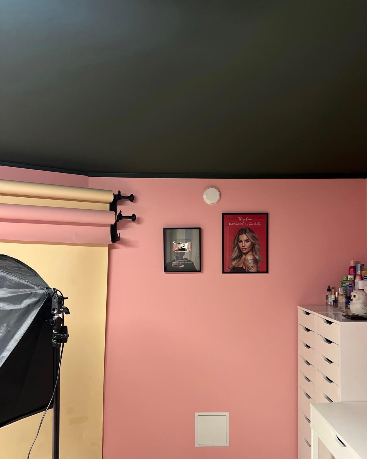 Rosa vägg med inramade tavlor och vit byrå under det mörkt målade taket
